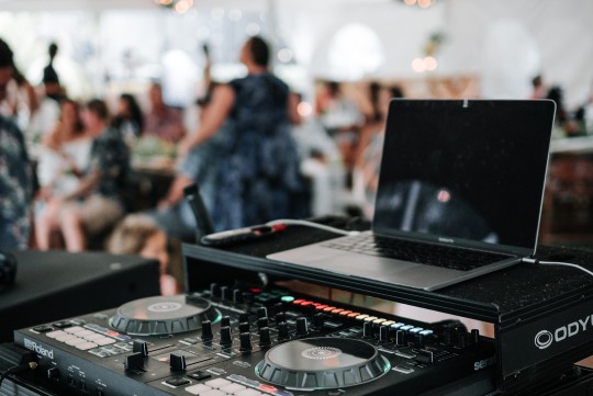 Image of DJ equipment with wedding guests in background.